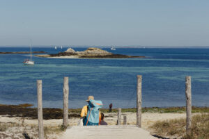 Randonneur avec sac à dos descendant vers une plage bretonne aux eaux turquoise en septembre