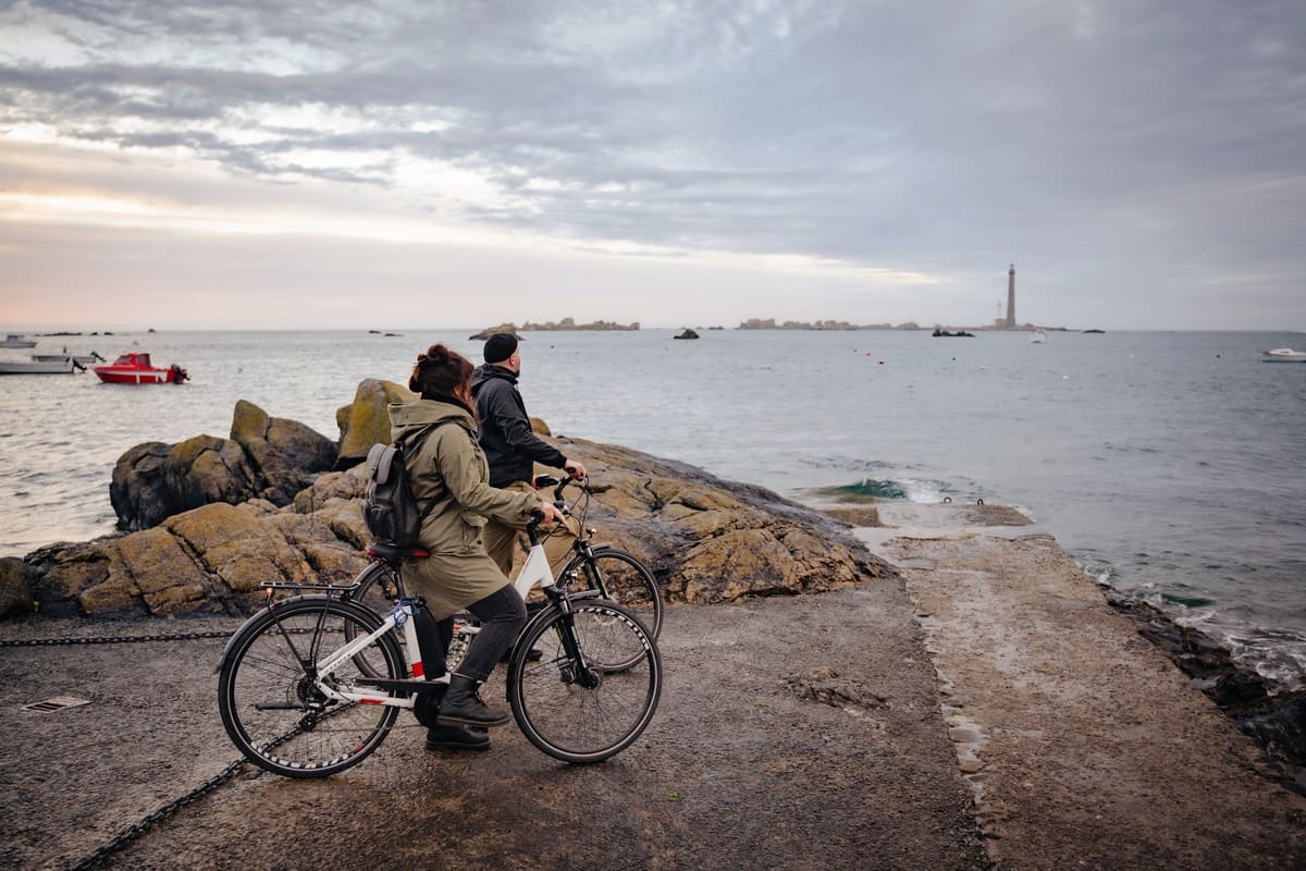 Couple de cyclistes observant le phare de l’île Vierge depuis le littoral du Finistère
