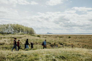 Groupe de randonneurs dans la baie du Mont-Saint-Michel avec vue sur l’abbaye au loin