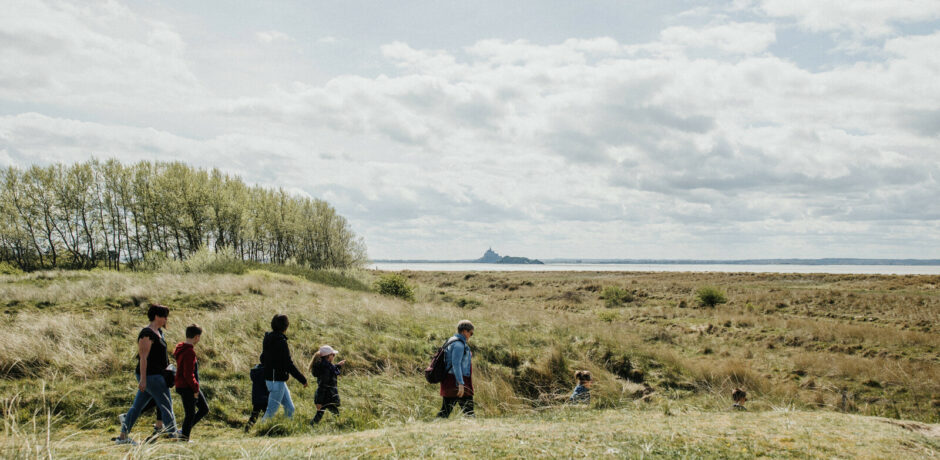 Groupe de randonneurs dans la baie du Mont-Saint-Michel avec vue sur l’abbaye au loin
