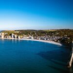 Panorama aérien sur Étretat et sa plage de galets, entourée des falaises blanches emblématiques de la Côte d’Albâtre en Normandie.