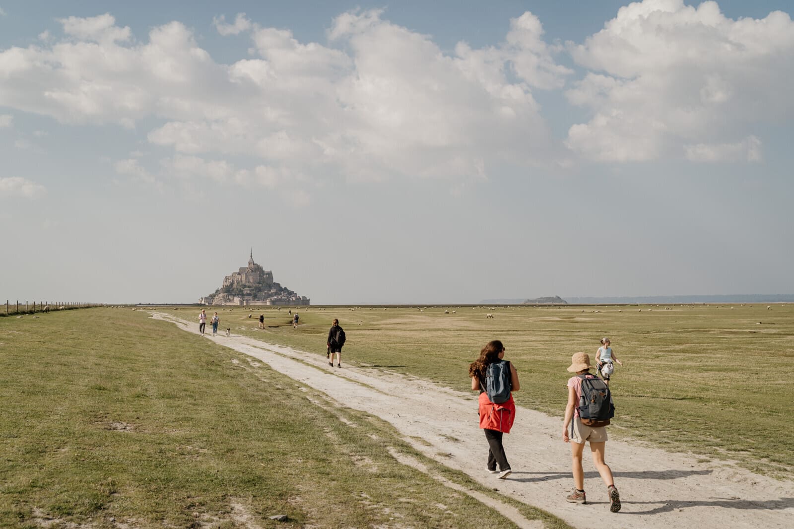 Randonneurs en marche vers le Mont Saint-Michel à travers les herbus