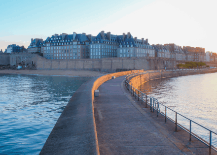 Jetée courbe menant aux remparts de Saint-Malo, bordée par la mer et éclairée par un soleil rasant.