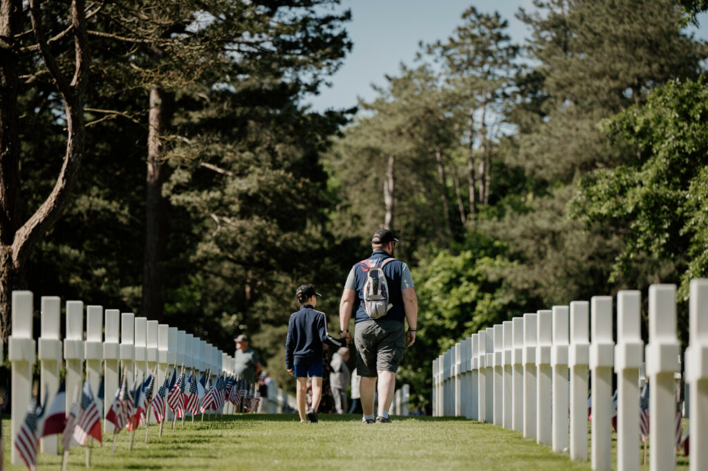 Père et fils marchant entre les croix blanches du cimetière militaire américain de Colleville