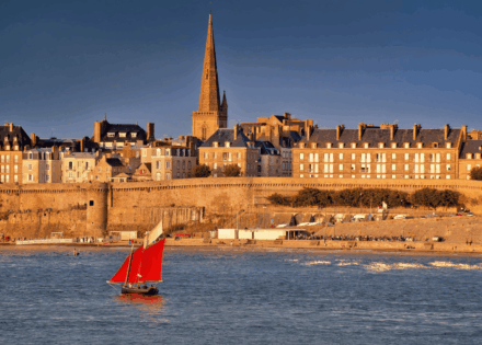 Voilier traditionnel aux voiles rouges devant les remparts de Saint-Malo au coucher du soleil