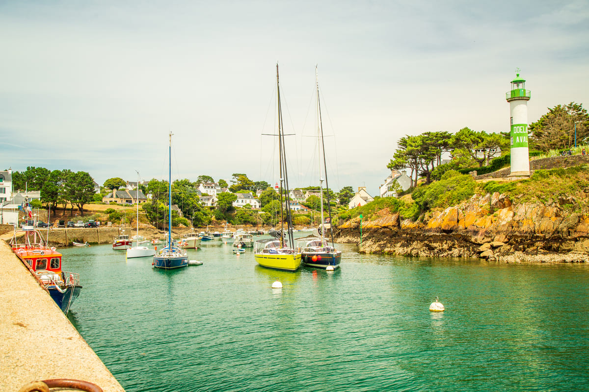 Port de Doëlan animé en été avec bateaux, voiliers et phare aval