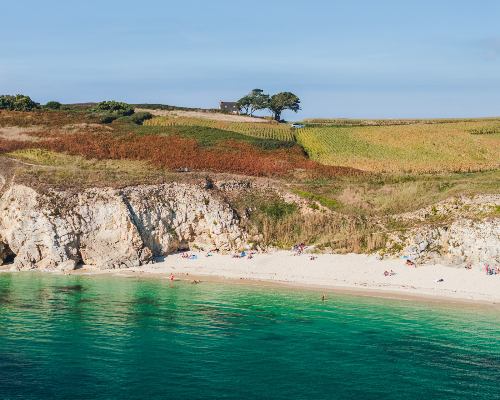Plage sauvage aux eaux turquoise bordée de falaises et champs colorés dans les Abers, Finistère.
