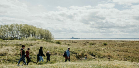 Groupe de randonneurs dans la baie du Mont-Saint-Michel avec vue sur l’abbaye au loin