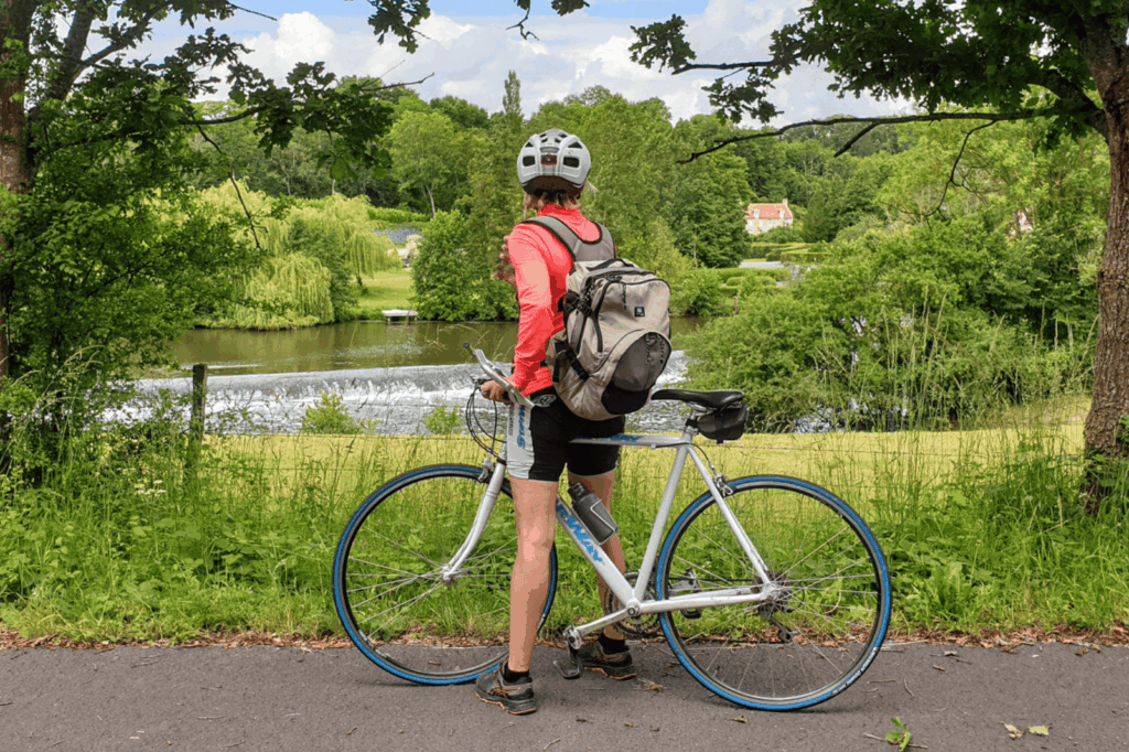 Cycliste de dos admirant la rivière et le paysage verdoyant sur la voie verte en Suisse Normande.