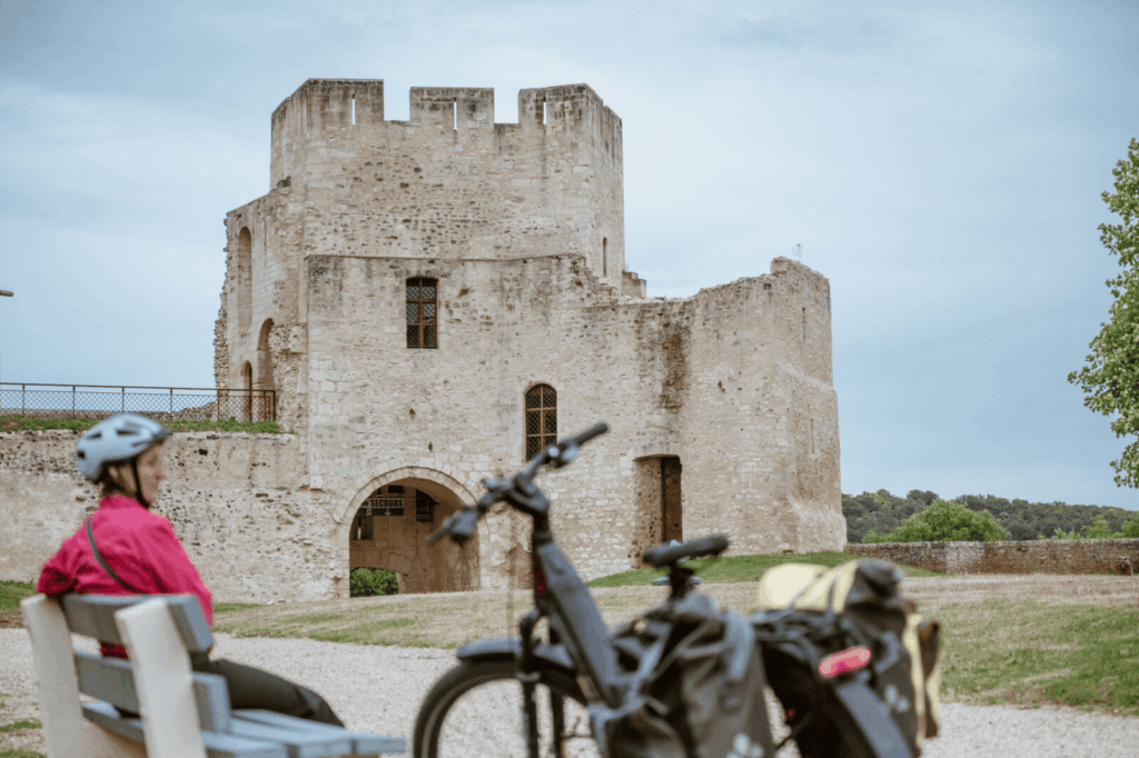 Cycliste assise sur un banc observant le Château de Gisors en arrière-plan.
