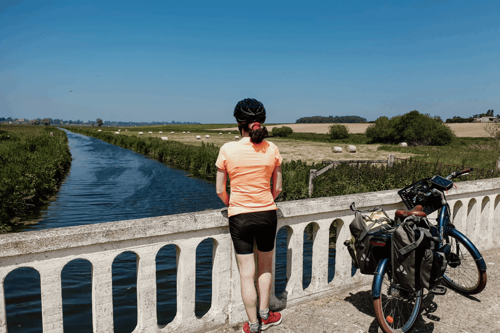 Cycliste accoudée au pont de Janville regardant la rivière la Dives et la plaine.