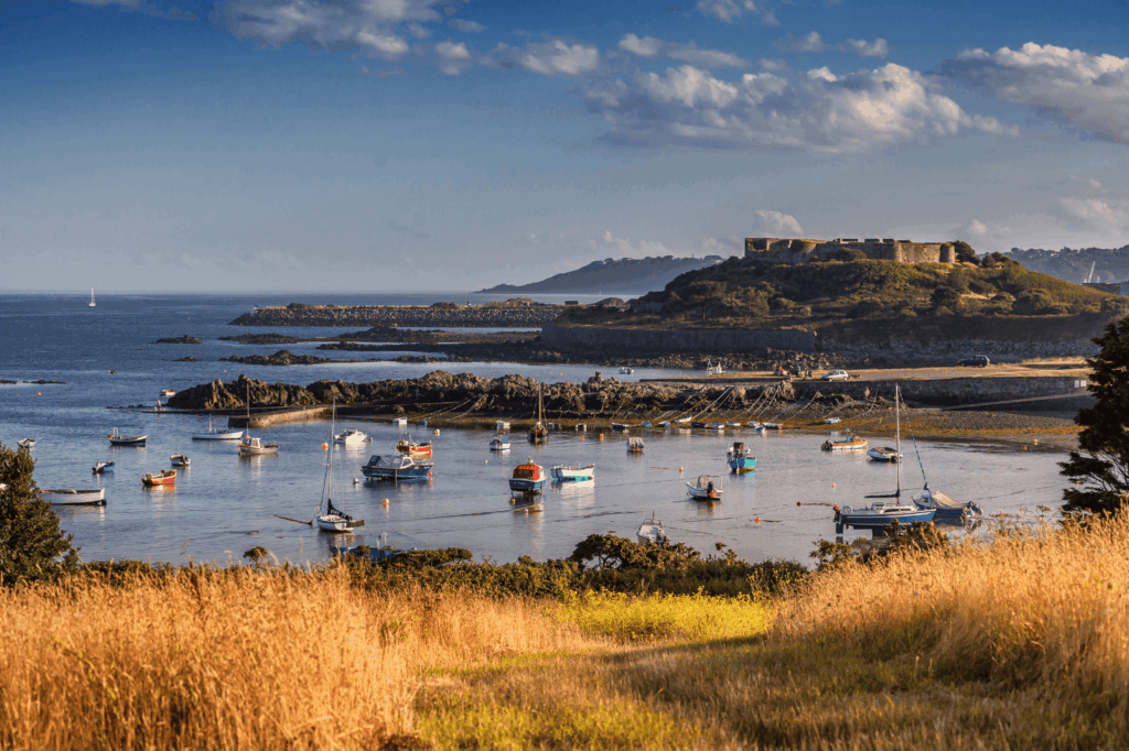 Port pittoresque de Guernesey à marée basse avec bateaux colorés et château fortifié en arrière-plan