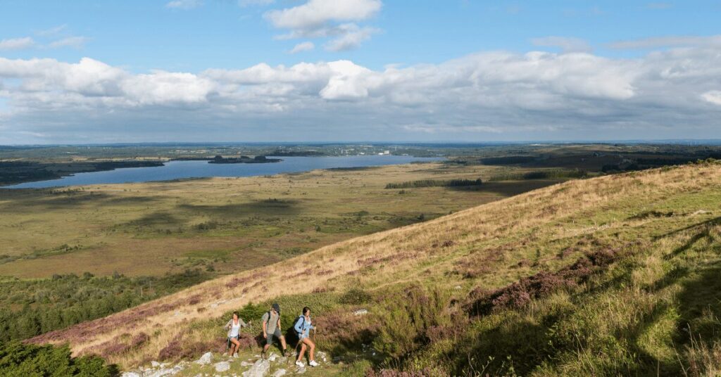 Trois randonneurs sur une crête de lande dominant un lac et des forêts à l'intérieur de la Bretagne